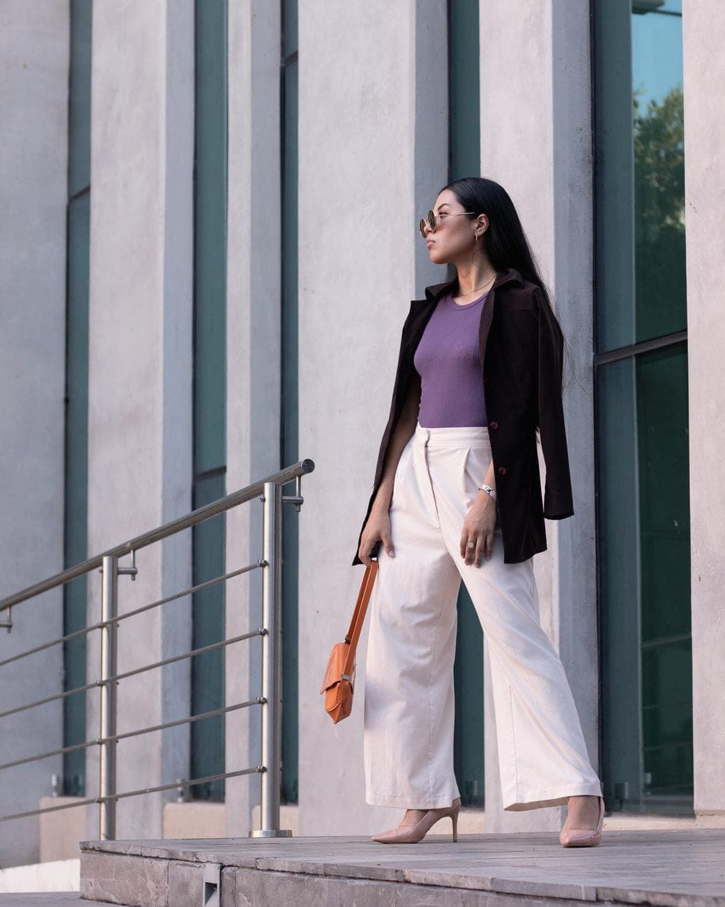 Vrouw in een witte wijde pantalon, een paarse top en een zwarte blazer voor een kantoorgebouw