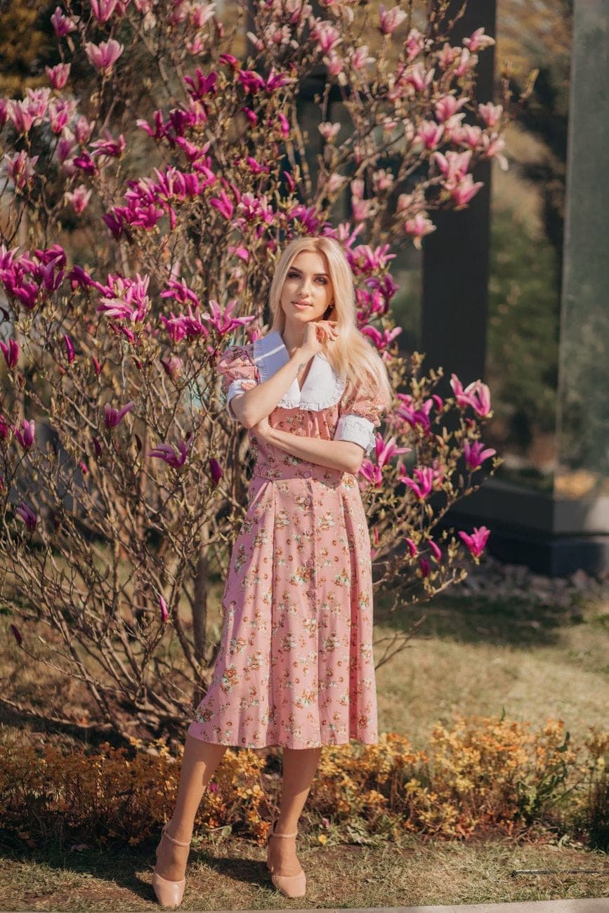Vrouw in een roze midikleed met bloemenprint tussen bloeiende magnolia's