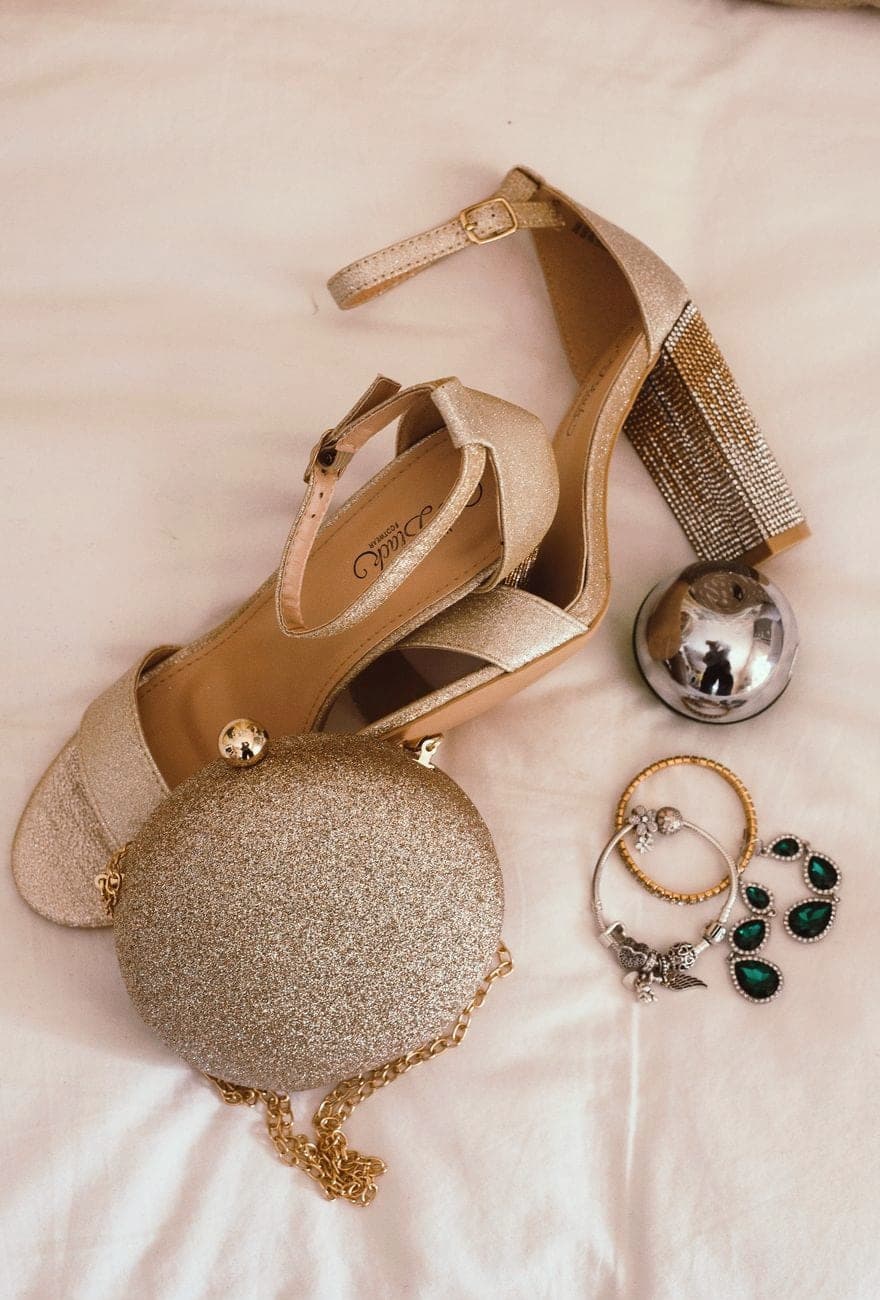 Beige sandalen met hak, een ronde glittertas en sieraden op een laken